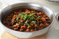 Bowl of chili with ground soya, beans, and vegetables on a wooden cutting board.